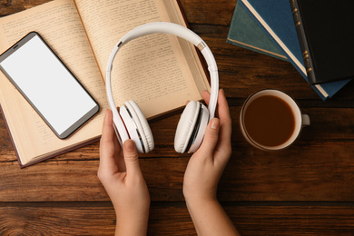 Photo of Woman holding headphones over wooden table with books, top view
