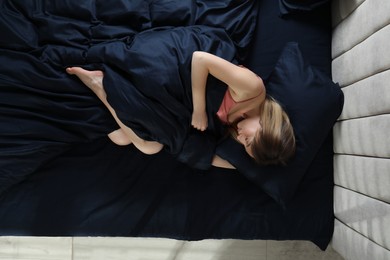 Photo of Young woman sleeping in comfortable bed with silky linens, top view