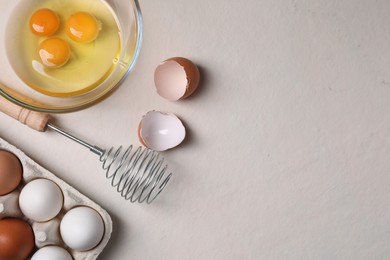 Photo of Metal whisk, raw eggs and shells on light table, flat lay. Space for text