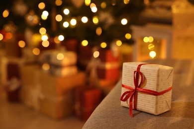 Christmas gift box on sofa against blurred lights indoors. Space for text