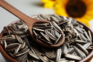 Photo of Raw sunflower seeds and wooden spoon in bowl, closeup