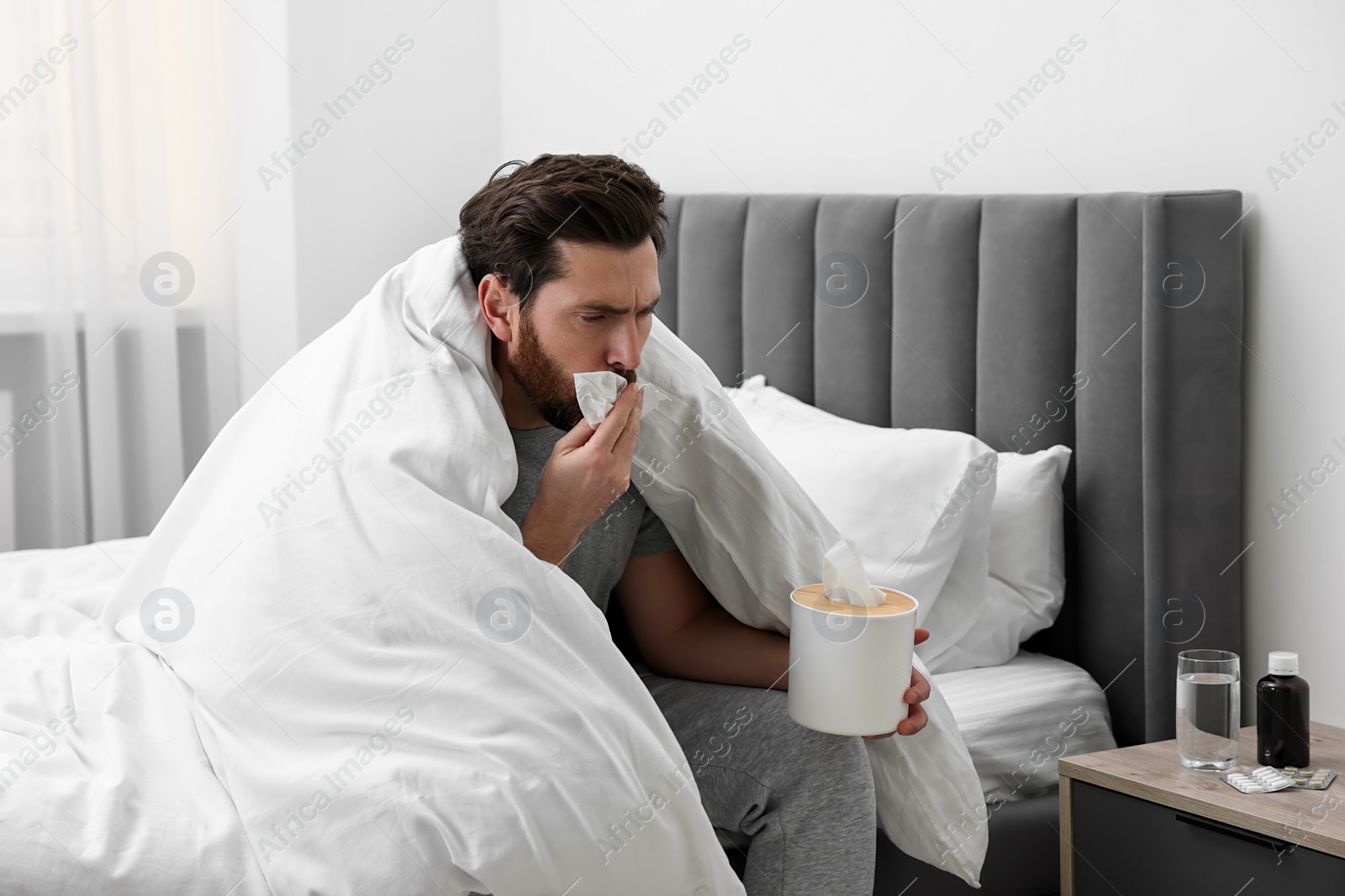 Photo of Sick man with tissue coughing on bed at home. Cold symptoms