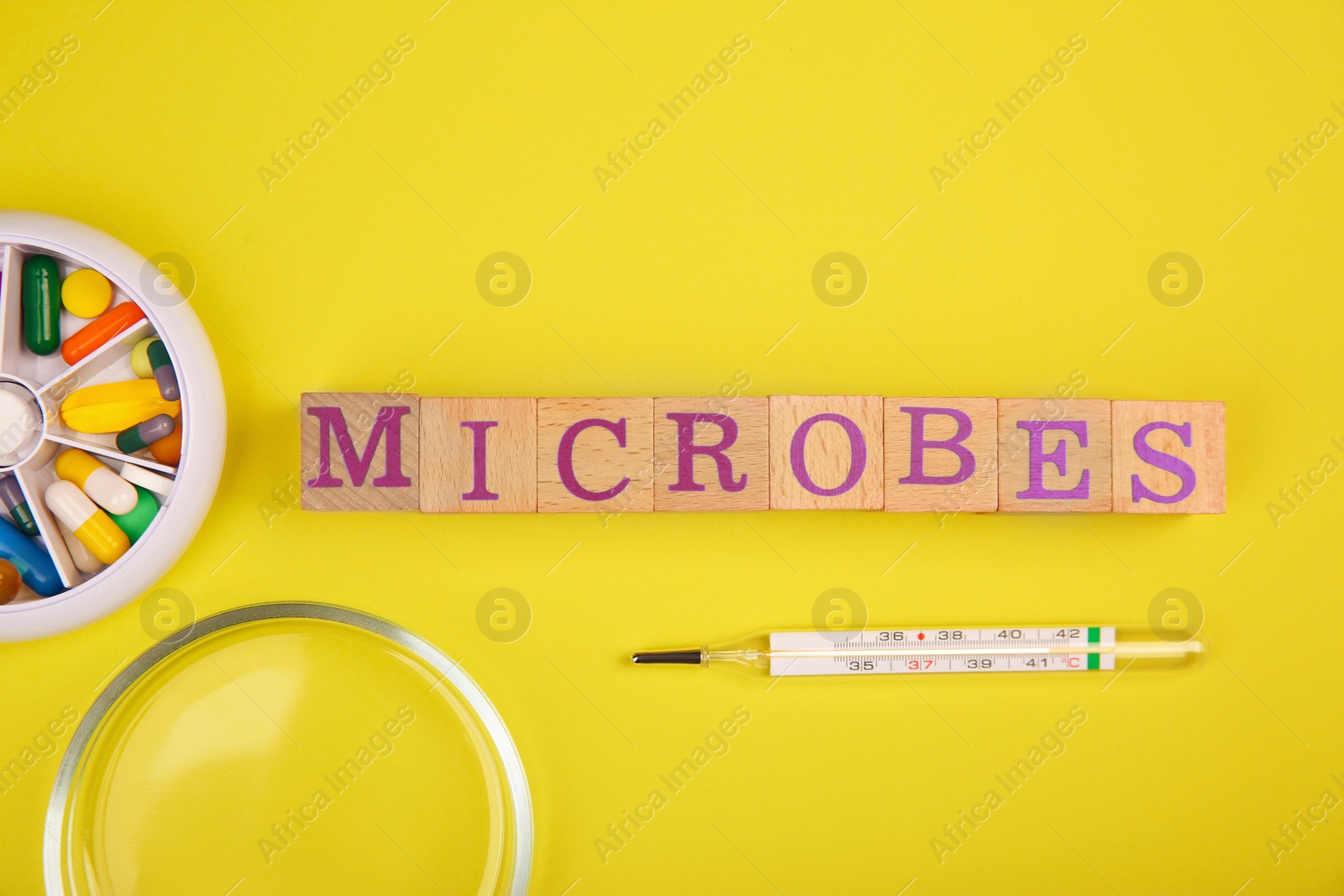 Photo of Word Microbes made with wooden cubes, syringe, pill box and magnifying glass on yellow background, top view