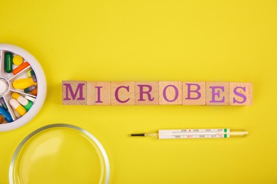 Photo of Word Microbes made with wooden cubes, syringe, pill box and magnifying glass on yellow background, top view