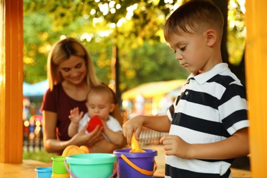 Photo of Nanny and cute children playing with toys outdoors. Space for text