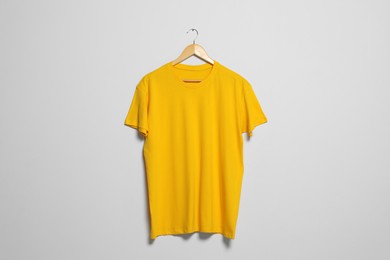 Hanger with yellow t-shirt on light wall. Mockup for design
