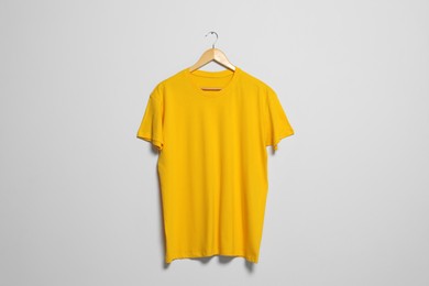 Photo of Hanger with yellow t-shirt on light wall. Mockup for design