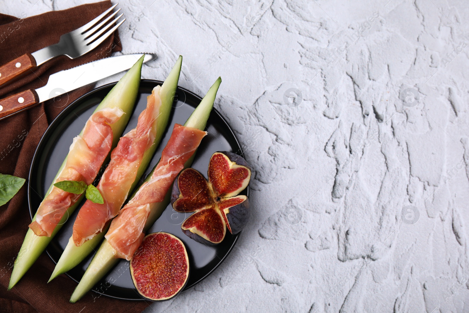 Photo of Tasty melon, jamon and figs served on white textured table, flat lay. Space for text