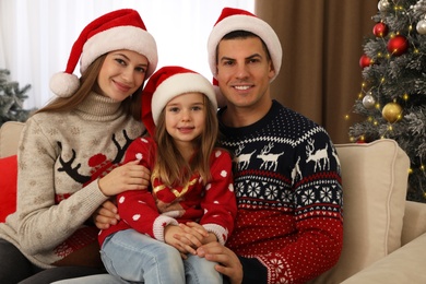 Happy family in Santa hats near Christmas tree at home