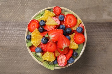 Photo of Delicious fresh fruit salad in bowl on wooden table, top view