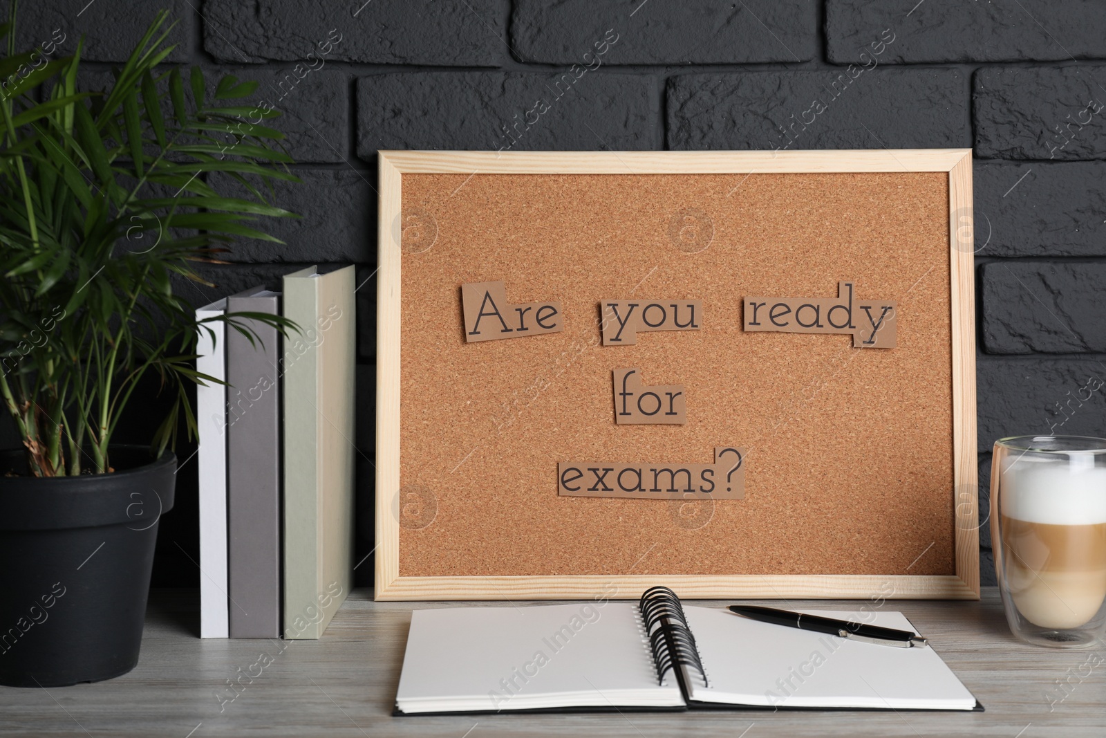 Photo of Cork board with phrase Are You Ready For Exams? on wooden table near black brick wall