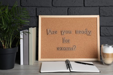 Photo of Cork board with phrase Are You Ready For Exams? on wooden table near black brick wall