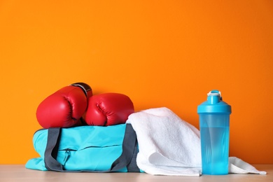 Photo of Sports bag, boxing gloves, towel and bottle of water on wooden table against color background