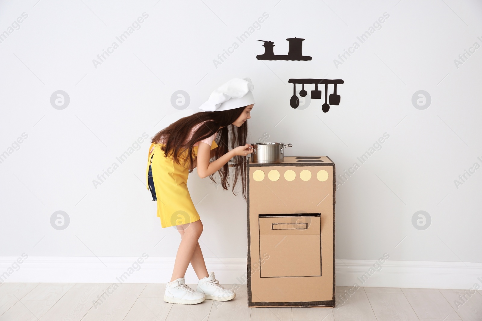 Photo of Little child in chef hat playing with carton stove indoors