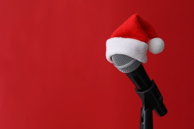 Photo of Microphone with Santa hat on red background, space for text. Christmas music