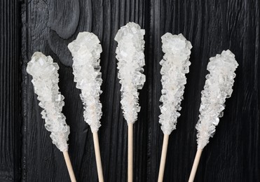 Sticks with sugar crystals on black wooden table, flat lay. Tasty rock candies