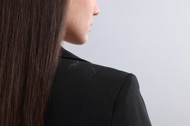 Woman with dandruff on her jacket against light grey background, closeup. Space for text