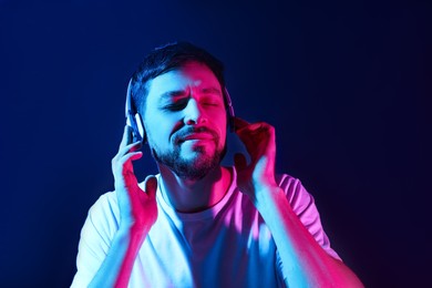Photo of Handsome man in headphones enjoying music in neon lights against dark blue background