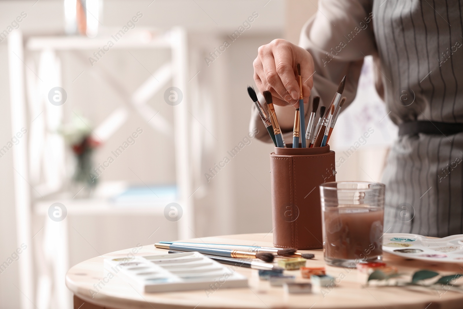 Photo of Watercolorist taking brush from holder on table in workshop, closeup