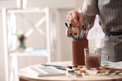 Watercolorist taking brush from holder on table in workshop, closeup