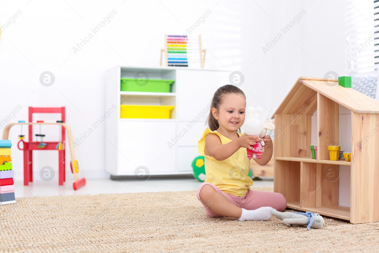 Photo of Cute little playing with toys near wooden house on floor at home, space for text