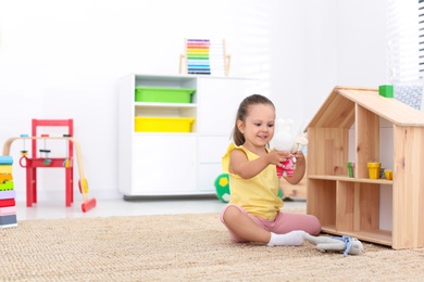 Photo of Cute little playing with toys near wooden house on floor at home, space for text