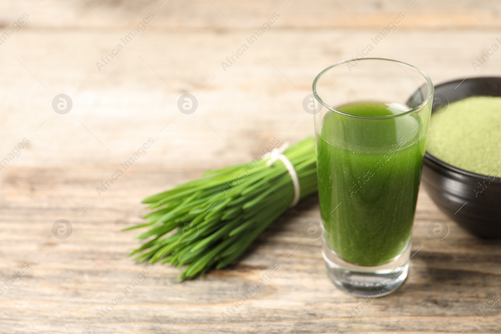 Photo of Wheat grass drink in shot glass and fresh green sprouts on wooden table, closeup. Space for text