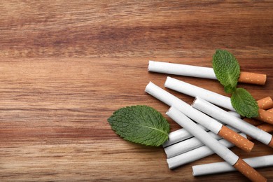 Photo of Menthol cigarettes and mint leaves on wooden table, flat lay. Space for text
