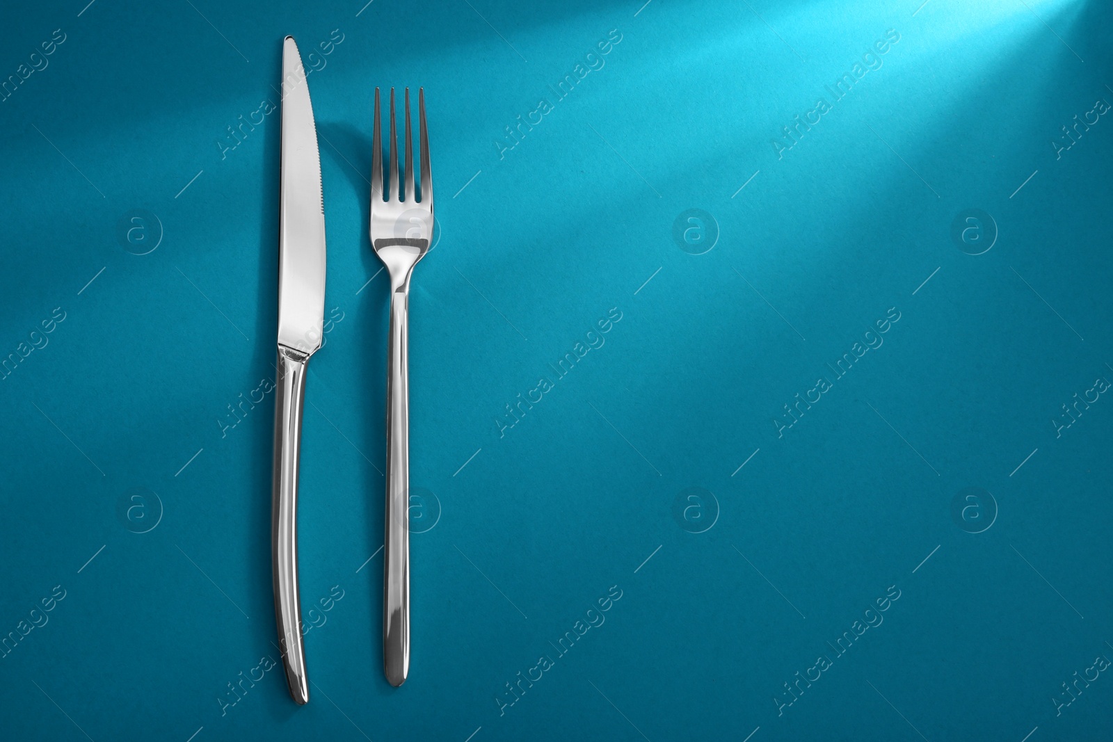 Photo of Shiny fork and knife on light blue background, flat lay. Space for text