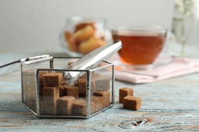 Photo of Glass bowl with brown sugar cubes on wooden table. Space for text