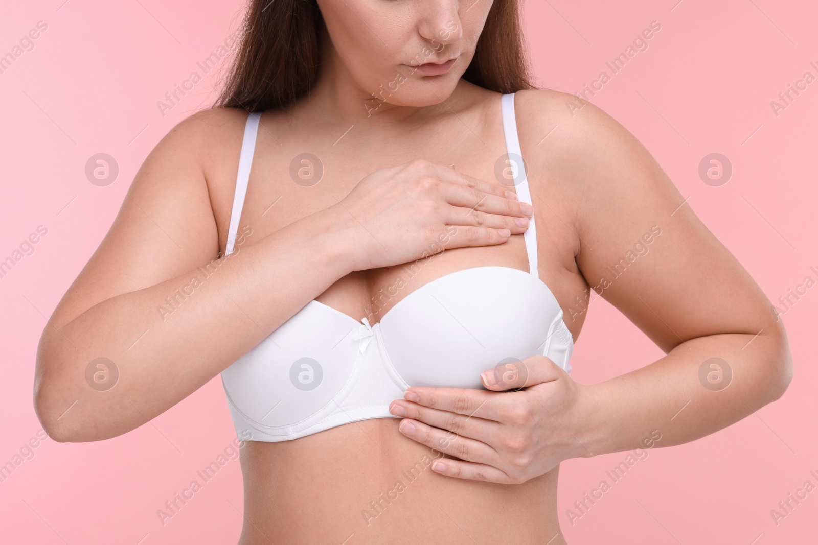 Photo of Mammology. Woman in bra doing breast self-examination on pink background, closeup