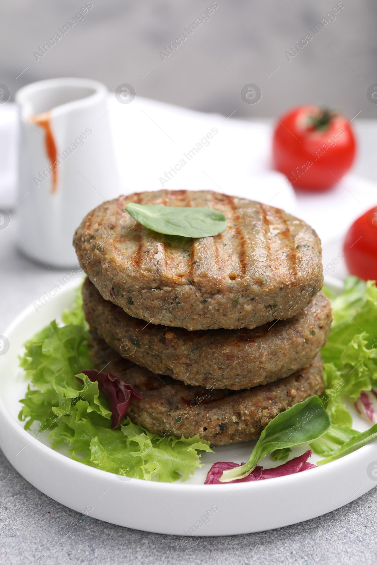 Photo of Delicious grilled vegan cutlets, lettuce and spinach on light grey table, closeup