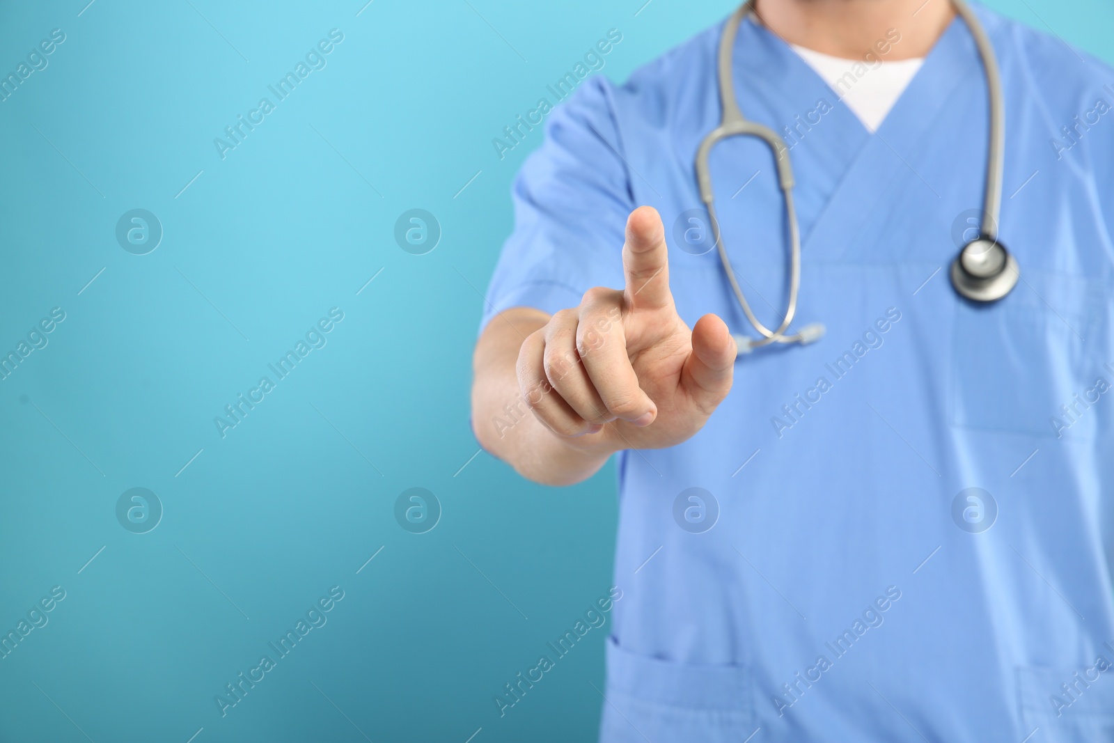 Photo of Doctor with stethoscope pointing at something on light blue background, closeup. Space for text