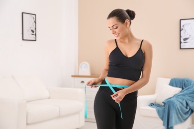 Photo of Slim woman measuring her waist at home, space for text. Weight loss