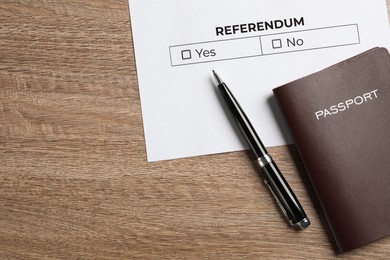 Photo of Referendum ballot with pen and passport on wooden table, flat lay. Space for text