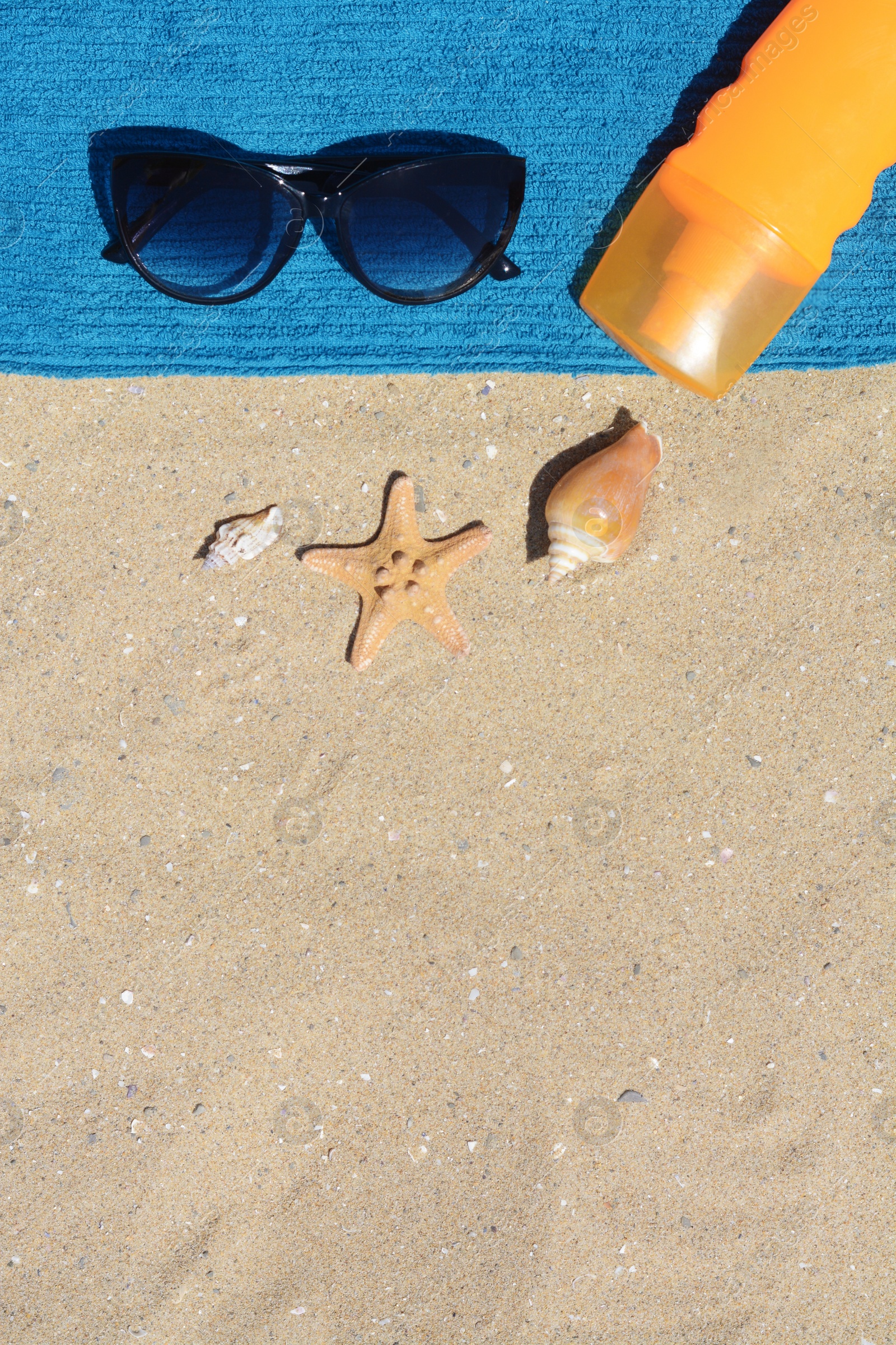 Photo of Stylish sunglasses, bottle of sunblock and blue towel on sand, flat lay with space for text. Beach accessories