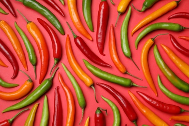 Different colorful chili peppers on red background, flat lay