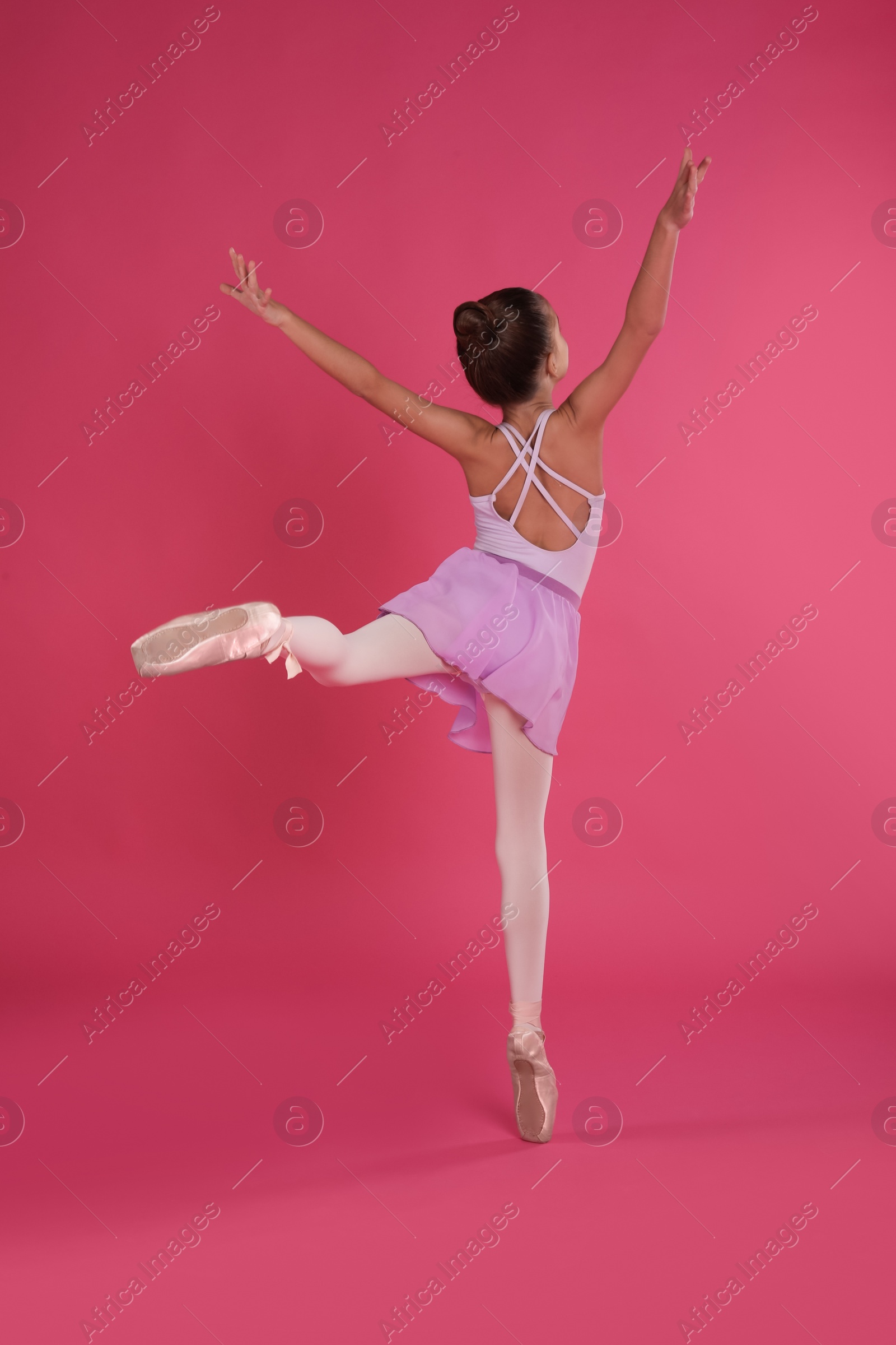 Photo of Little ballerina dancing on pink background, back view