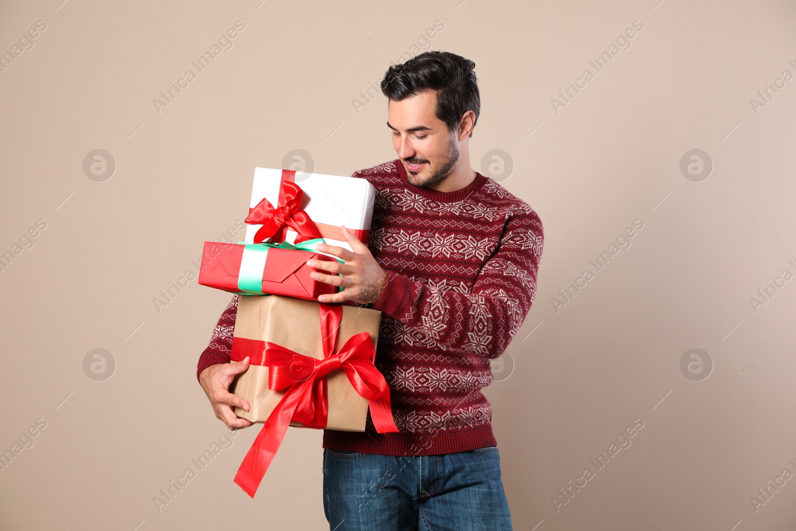 Photo of Happy man in Christmas sweater holding gift boxes on beige background