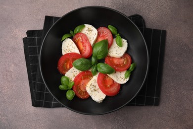 Photo of Caprese salad with tomatoes, mozzarella, basil and spices on brown table, top view