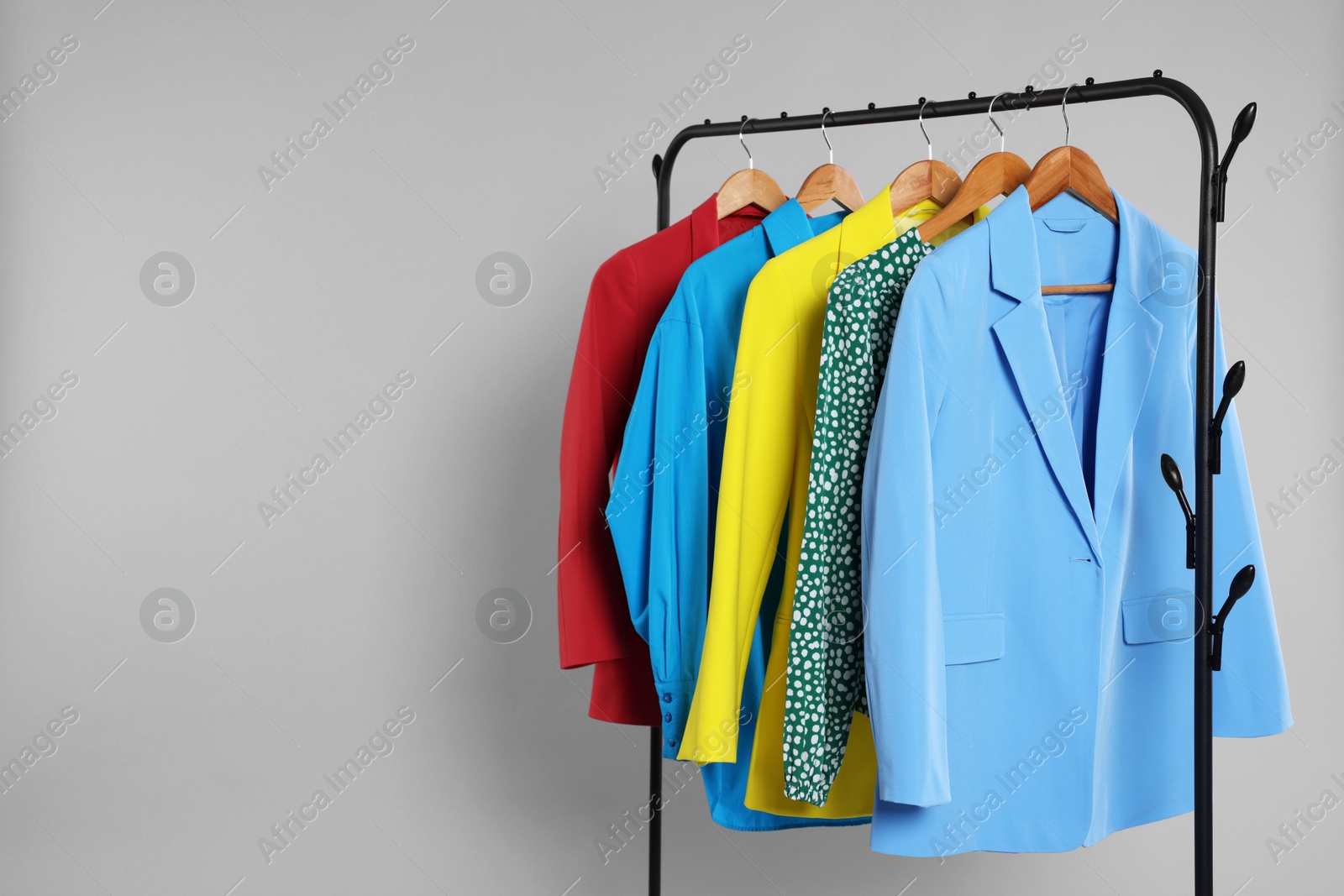Photo of Rack with stylish women`s clothes on wooden hangers against light grey background, space for text