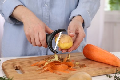 Woman peeling fresh potato at table indoors, closeup