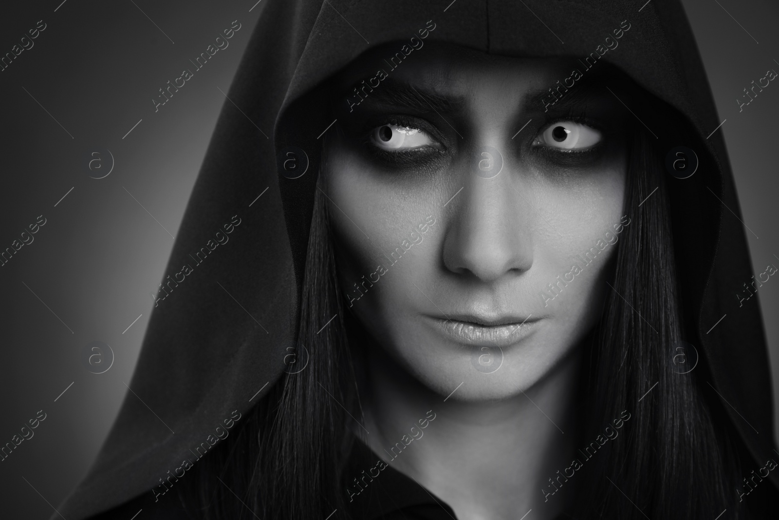 Photo of Mysterious witch with spooky eyes on dark background, closeup. Black and white effect