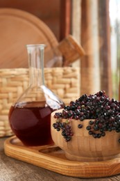 Elderberry wine and bowl with Sambucus berries on wooden table near window