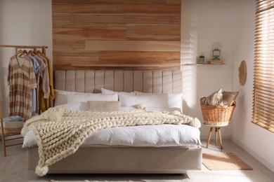 Bed with white knitted plaid in room. Interior design