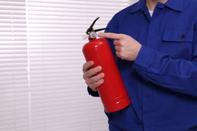 Photo of Man checking pressure and quality of fire extinguisher indoors, closeup. Space for text