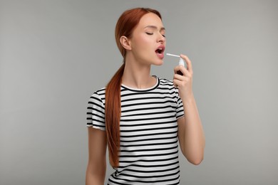 Photo of Young woman using throat spray on grey background