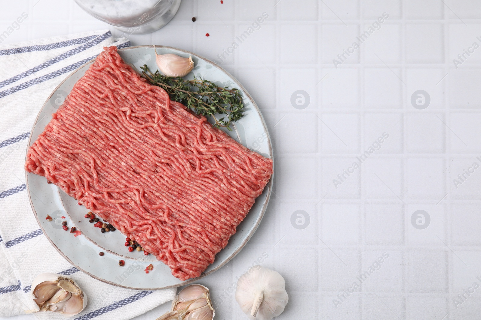 Photo of Fresh raw ground meat, peppercorns, garlic and thyme on white tiled table, flat lay. Space for text