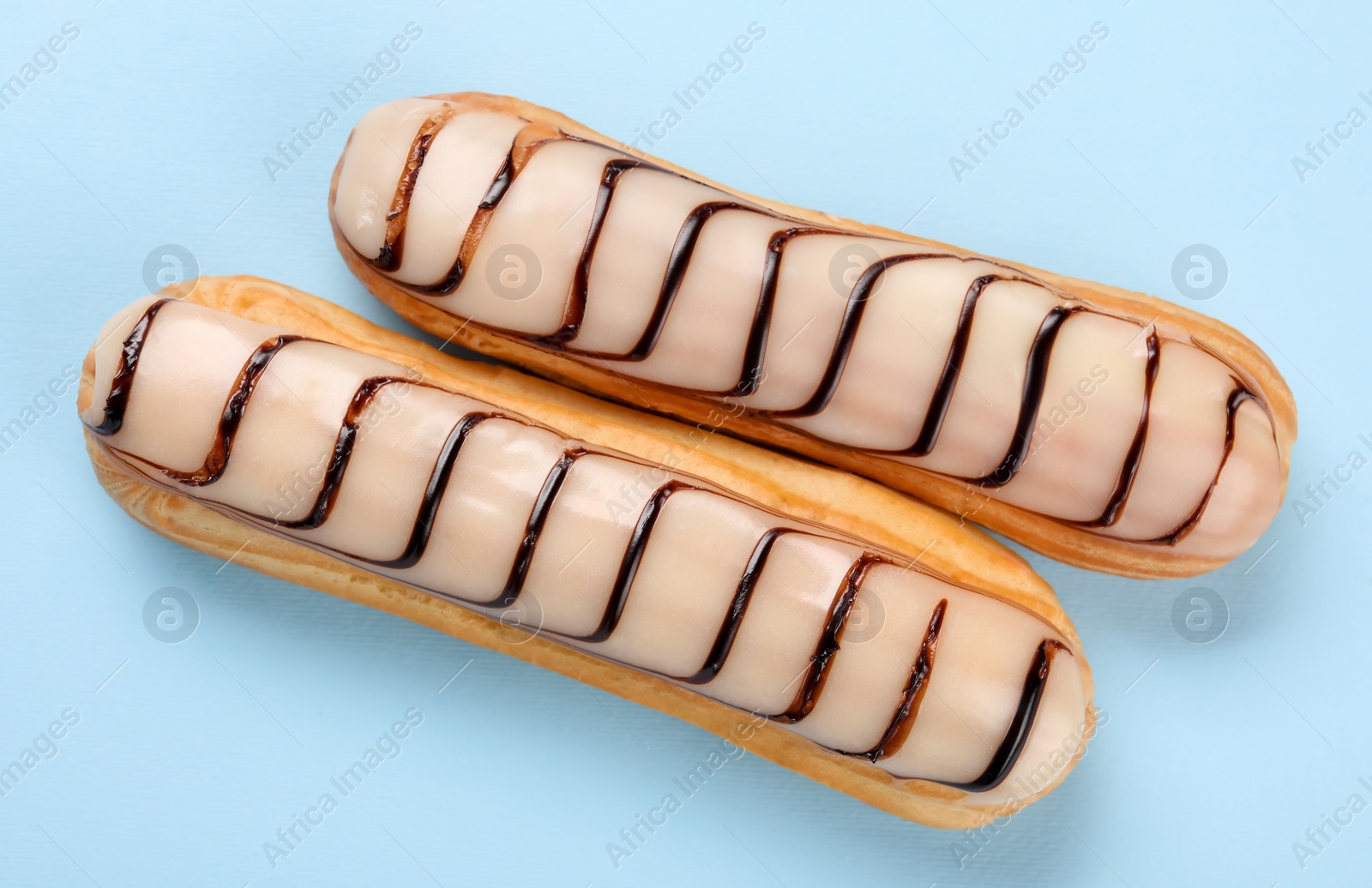 Photo of Delicious eclairs covered with glaze on light blue background, top view