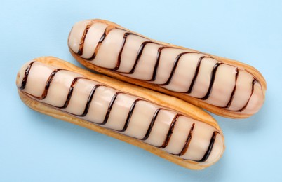 Photo of Delicious eclairs covered with glaze on light blue background, top view